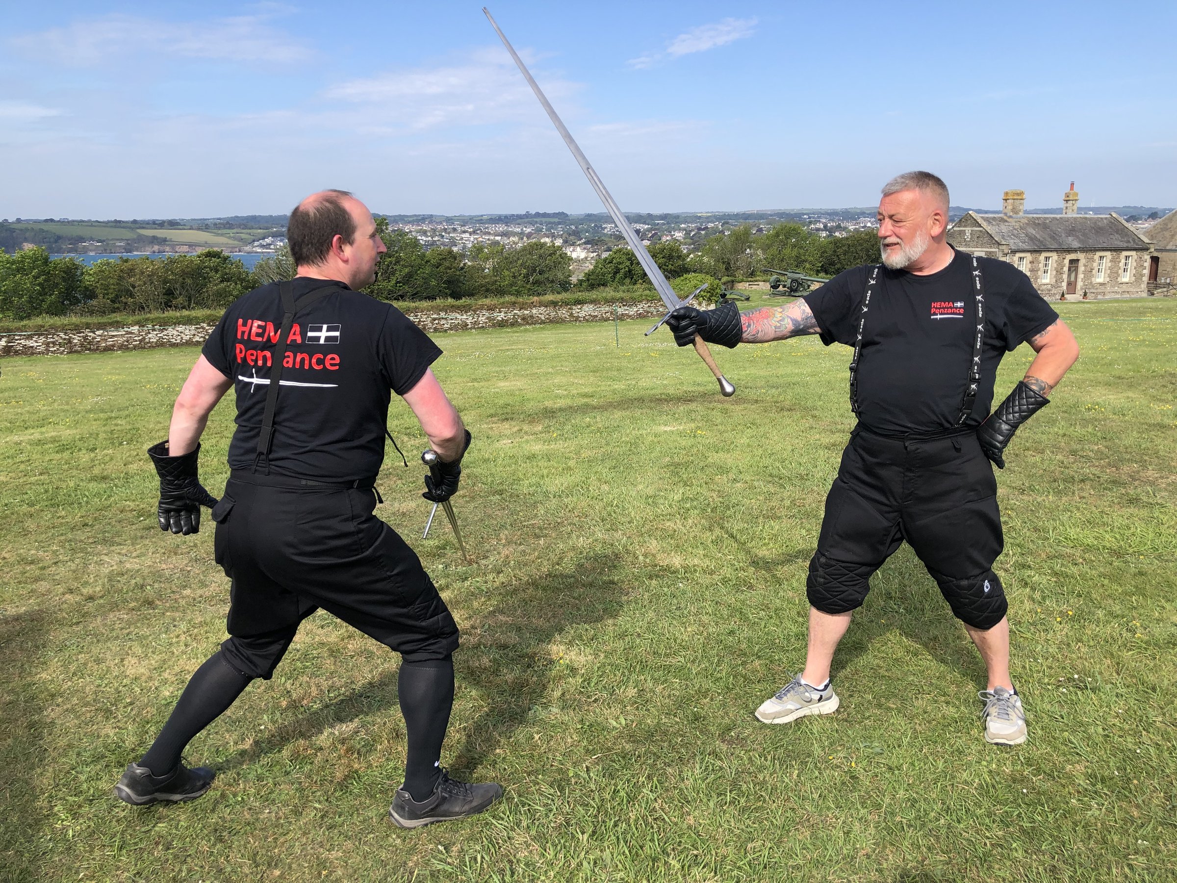 Two HEMA Penzance members sparring with longswords on the grass at Pendennis Castle